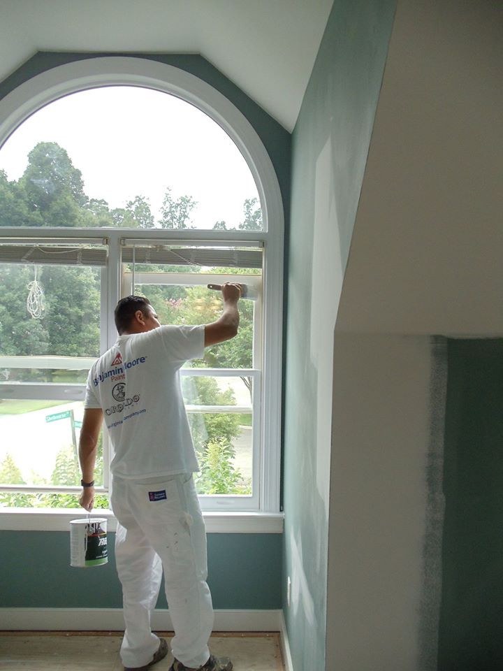 Painter cutting in around an arched window on an interior wall