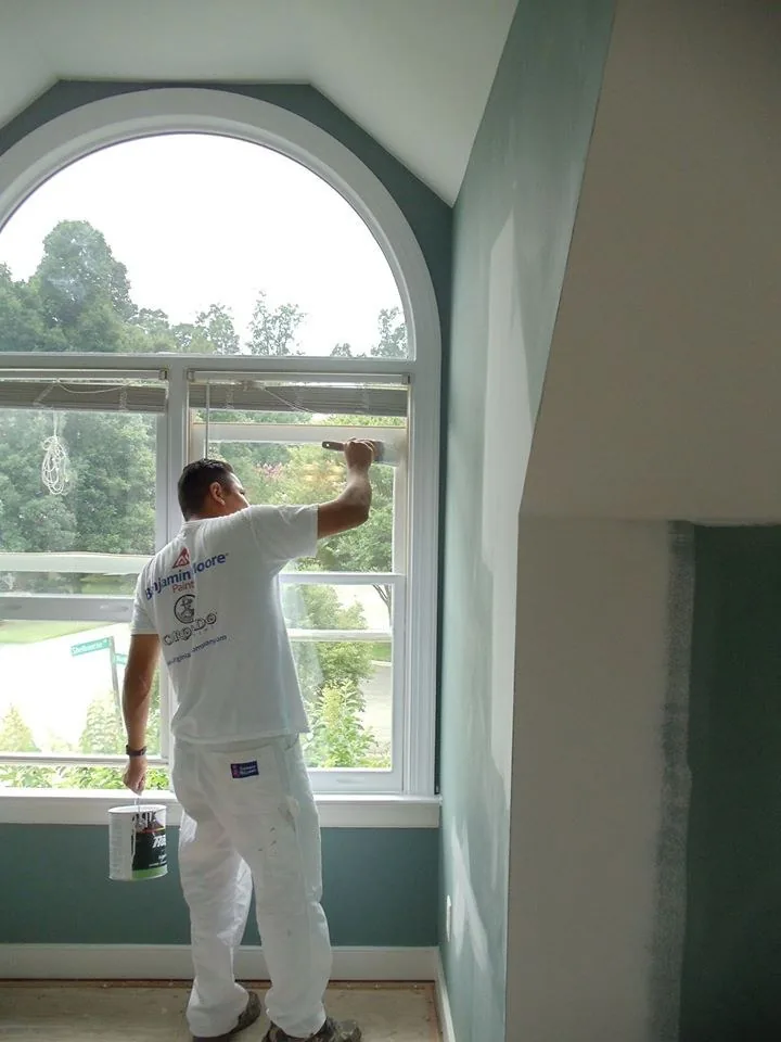 Painter cutting in around an arched window on an interior wall