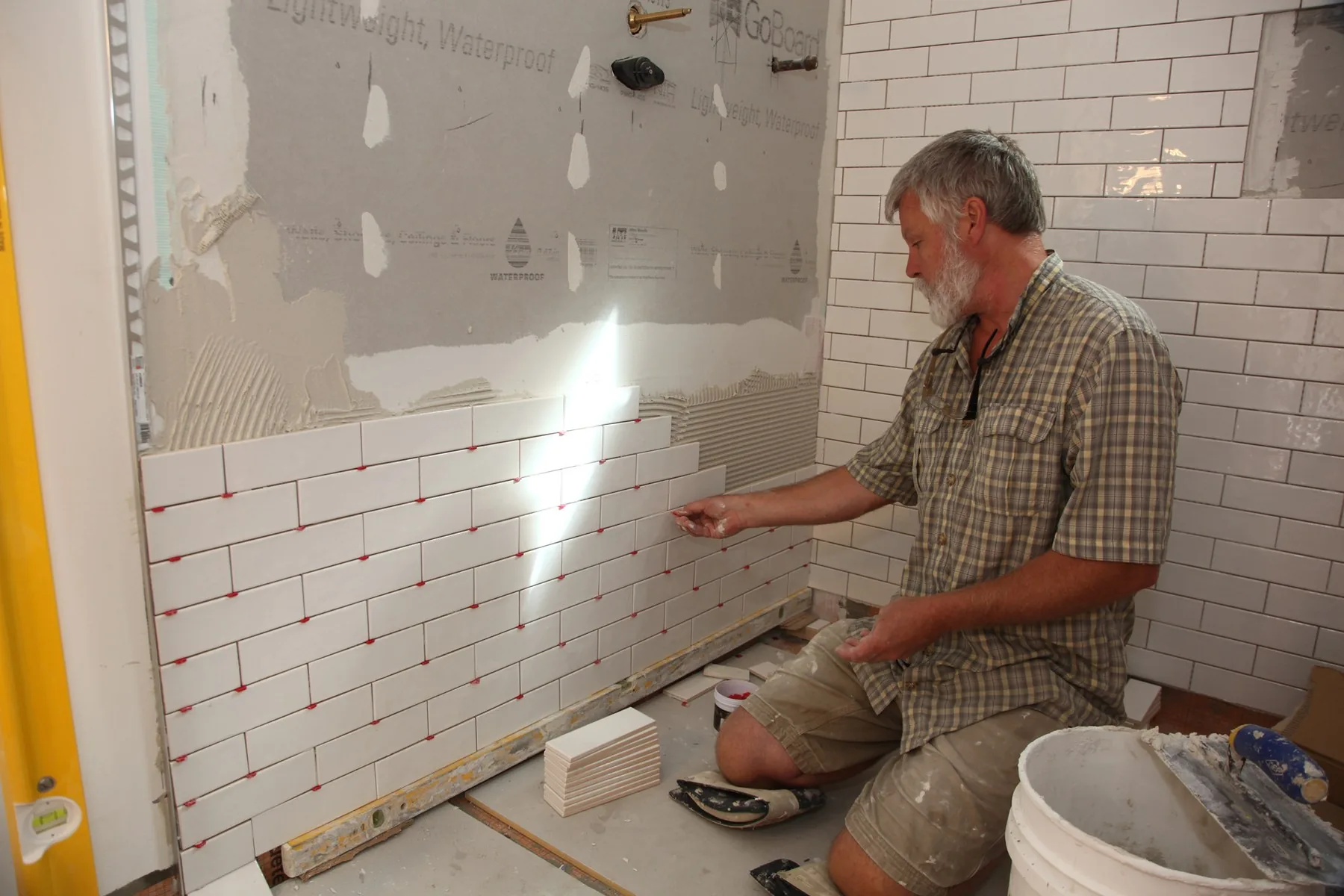 Tile setter installing white subway tile in a shower surround