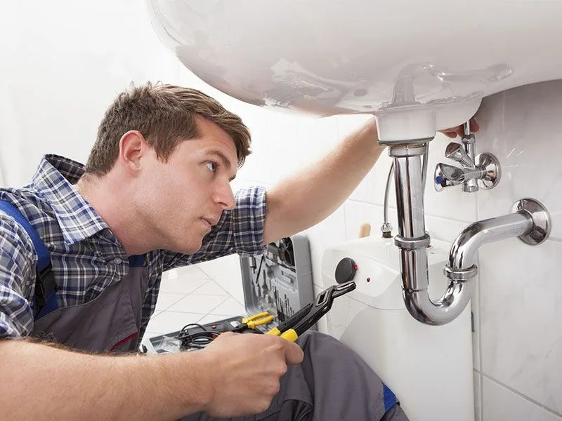 Technician replacing plumbing supply lines under a bathroom sink